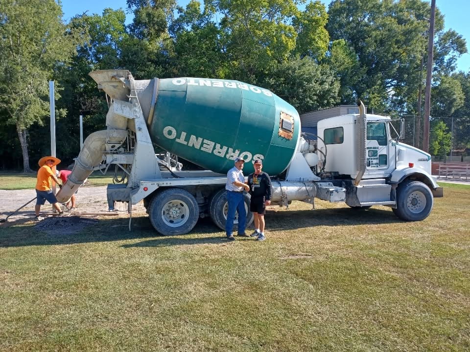 Green-drum Sorrento mixer truck delivering concrete for the Ascension Christian Schools softball batting cages